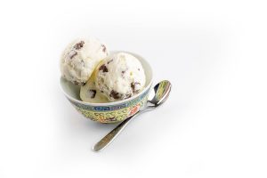 3 scoops of chocolate fudge ice cream in small bowl with spoon on white background